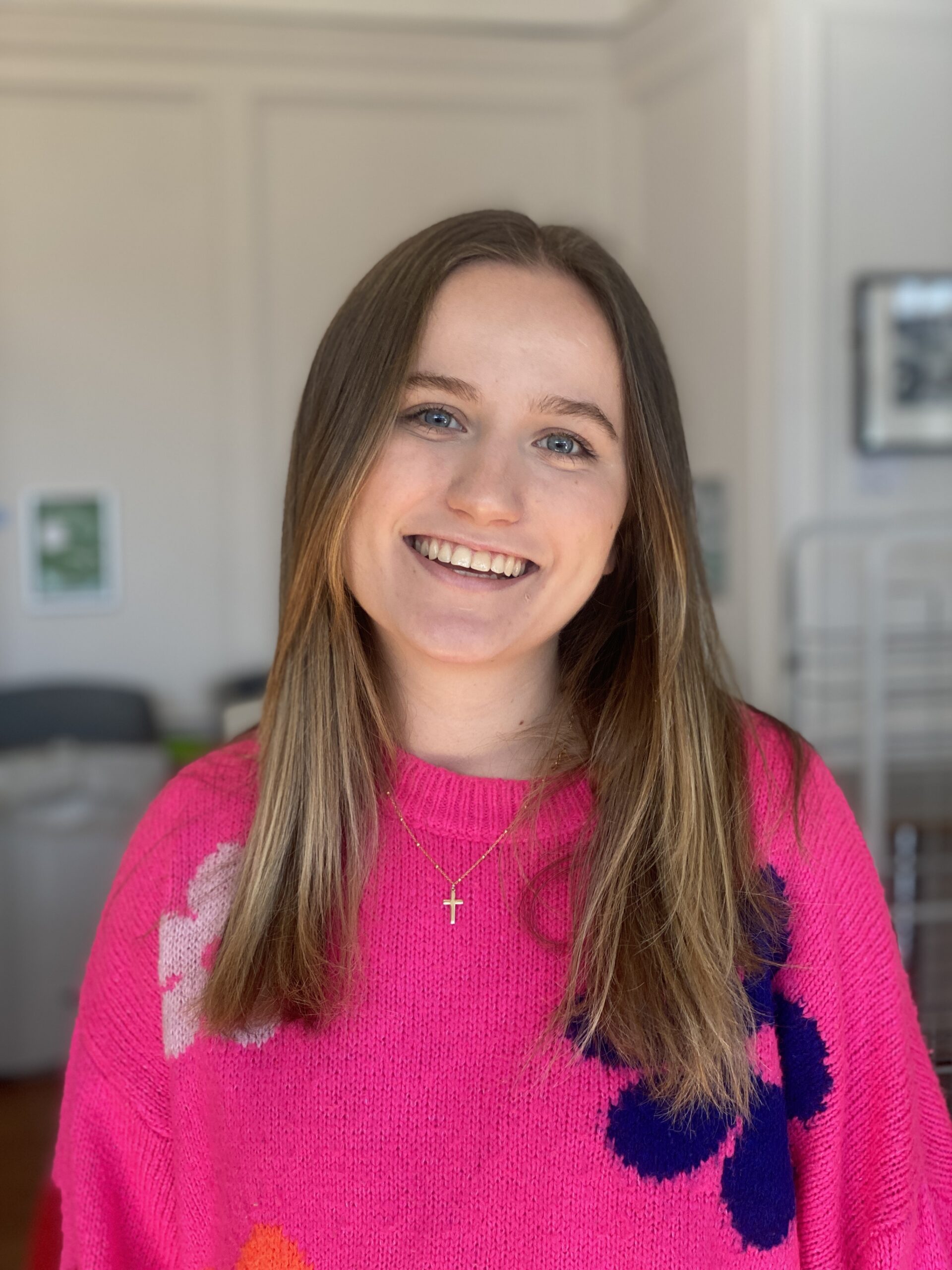 A young woman in a pink jumper smiles at the camera